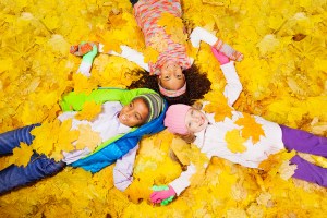 Three kids, girls and a boy laying on the ground covered with autumn maple orange leaves laying on the ground