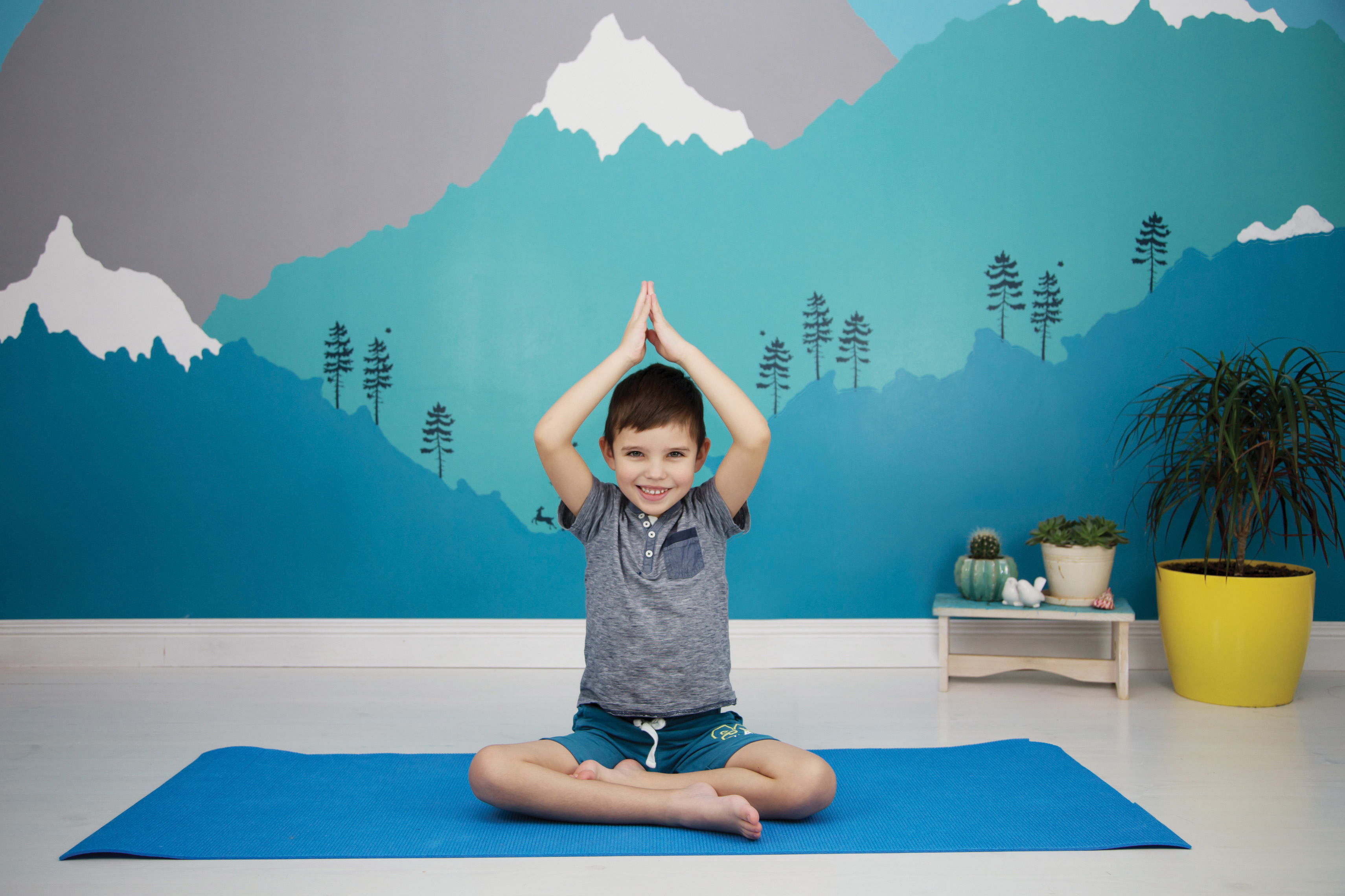 Cute caucasian child does yoga in his room with a beautiful moun